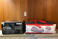 Thule rooftop bag cargo carrier box alongside Outbound 8-person tent in fabric carrying bag on shelf.