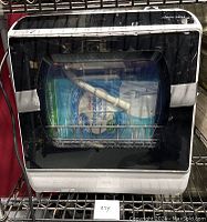 Front view of Airmsen dishwasher showing black door with transparent window, hose inside and dishwashing powder packaging visible.