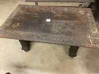 Angle top view of carved oak tabletop showing floral corner decorations and border pattern with signs of wear and damage.