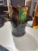 Side view of ceramic umbrella stand showing raised water lily and leaf motif with green, yellow, and brown glaze finish