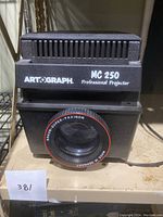 Front view of black Artograph MC 250 Professional Projector showing branding and large Braun Super-Paxigon lens with 'Made in Germany' marking.