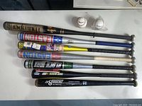 Full assortment of baseball and softball bats, showing worn condition and D1 Diamond baseballs on white surface.