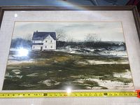 Framed watercolor painting signed by Richard Saunders showing a white two-story house in a landscape with barren trees and grass patches, framed with a cream mat and metallic wooden frame