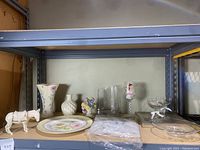 Wide shot showing the Lenox ceramic donkey, two small vases, anniversary glasses, plates, and handkerchiefs on shelf.