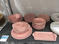 Full view of pink dishes including bowls, plates, and a rectangular tray arranged on shelf.