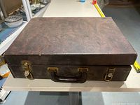 Closed vintage tool case showing dark brown textured exterior with leather handle and metal latches.