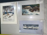 Three watercolor paintings mounted or framed: snowy woodland scene, waterfall, and seagulls.