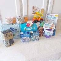 Overall lot showing all items including diapers, bottles, pacifiers, socks, thermometer, cup, and toy displayed together.