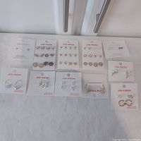 Full spread of 11 Joe Fresh cards showing 29 pairs of earrings and one ring on white branded cards, various designs and finishes.