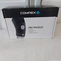 Photo of the boxed Compex Knee Pain Relief unit showing the product image and branding on the packaging.