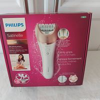 Front of box showing Philips Satinelle Prestige epilator with product image and feature highlights including ceramic discs for firm grip and wet/dry use.