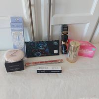 Full lot of makeup and skincare items including Laura Mercier powder and puff, Pacifica undereye masks, Uoma eyeshadow palette, Lancome mascara, Revolution Pro primer, Pink Make Up Eraser, Benefit brow pencil, and Bareminerals lip gloss balm.
