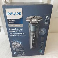 Front of sealed box showing Philips Series 5000 shaver with key features: powerful shave, gentle on skin, SteelPrecision blades, SkinIQ technology, 7-year motor and battery life.