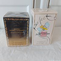 Both perfume boxes side by side: Marc Jacobs Daisy Eau So Intense (gold/black with floral design) and Marc Jacobs Perfect (white with illustration)