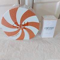 Michel Germain Sugarful & Spice round orange and white glitter swirled box and Givenchy L'Interdit white factory sealed box side by side.