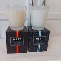 Two Nest Fragrances large scented candles in glass jars on top of their boxes, one Sicilian Tangerine with red-accented box and one Ocean Mist & Sea Salt with blue-accented box.