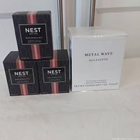 Photo showing three Nest New York Rose Noir & Oud scented candles in black decorative boxes and one Allsaints Metal Wave scented candle in a white sealed box.