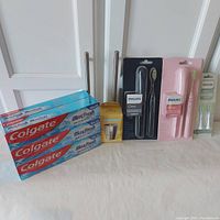 Photo showing all items including 2 toothbrushes (black and pink), 6 toothpaste tubes, mouthwash cup, and replacement brush heads