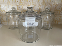 Four clear Anchor Hocking glass jars with lids arranged on countertop, showing full lot contents, size and style.