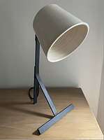Side view of the desk lamp showing white ceramic shade and black metal base on wooden surface.