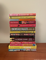 Side view of 14 stacked books showing titles and authors.