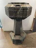 Full view of the aged metal holy water font showing the octagonal top, pedestal base, and overall condition.