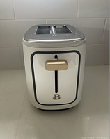 Front view of white and gold 2-slice toaster showing vertical slider lever and 'B' branding.