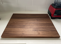 Top view of the rectangular walnut cutting board on a kitchen counter near a blender showing the wood grain and finish.