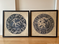 Both framed artworks side by side showing the two distinct blue and white plate designs in square wooden frames.