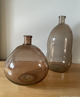 Pair of amber hand-blown glass vases on wood surface against white wall, showing comparative size and shape.