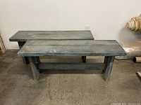 Two matching painted wooden benches placed on concrete floor against a white wall, showing the benches' full length and basic design.