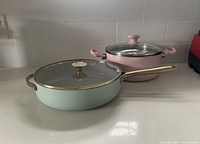 Masterclass 11-inch frypan with gold accented handle and lid knob, matte light green finish, accompanied by pink nonstick pot with matching lid and pink handles.