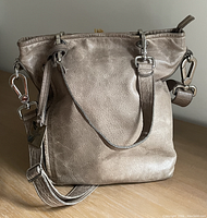 Taupe textured leather Rudsak shoulder/crossbody bag with metal hardware, two short handles, detachable adjustable strap, and zipper closure.