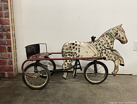 Side view of a vintage Tots Toys pedal car shaped like a horse with red metal frame and black seat.