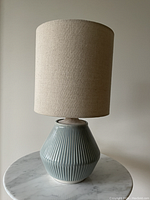 Front view of the West Elm lamp showing ceramic ripple texture body in muted blue-gray and wood base with natural finish, topped with natural linen cylindrical shade.