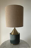 Front view of the West Elm table lamp showing turquoise ribbed base, gold metal cone, and beige linen shade.