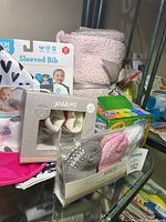 Photo of baby blanket, sleeved bibs, Udderz baby slippers, baby socks in packaging, and Crayola chalk on glass shelf