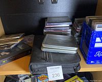 Shelf displaying a blue plastic crate with CDs and metal cases, zipped fabric case in front, and stacked CDs behind.