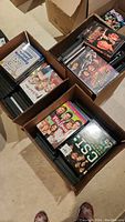 Four cardboard boxes filled with DVDs showing various titles including Full House, CSI, Starship Troopers, and others.