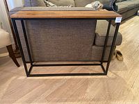 Full view of rectangular end table showing wood top and black iron frame against couch background.