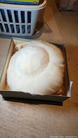 White round fur hat on tissue paper inside box