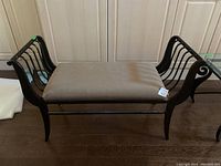 Front view of the heavy iron bench with beige upholstered seat placed on a wood floor in front of cabinets.