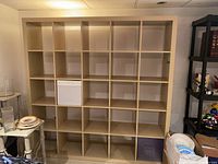 Front view of the large light wood bookcase showing all shelves and storage cubes with surrounding room area.