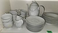 Photo of white fine china cups, creamer, and stacked plates on shelf.