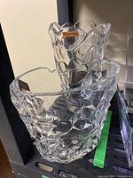 Pair of clear Nachtmann crystal vases featuring original brand labels and distinct sculptural designs on a black shelf.