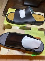 Pair of black leather Naot sandals with wide single strap on green Naot box, size 41 visible on inner sole