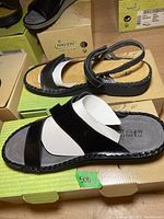 Side and top view of Naot women's black leather strap sandal on its box showing size 39 and brand markings.