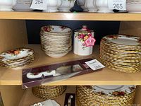 Second shelf overview showing stacks of bowls and plates, cylindrical lidded canister at center, boxed cake server and cutter set at front