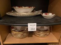 Photo of stacked small plates with floral rose pattern and gold trimmed edges, below larger bowls.