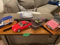 View of all five car figures and display case set on wooden bases and plastic cases placed on couch-side table.
